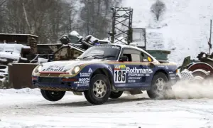 Porsche 959 w barwach Rothmans, z numerem 185, pokonuje śnieżny odcinek rajdu, wzbijając tumany śniegu.