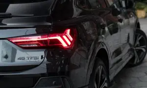 Czarne Audi Q3 45 TFSI quattro z zapalonymi światłami LED. Zbliżenie na tylną część pojazdu, podkreślające jego sportowy charakter i wymiary.