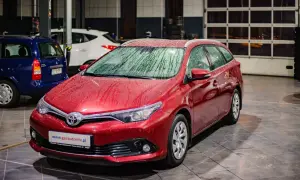 Czerwona Toyota Auris 1.6 benzyna z kroplami deszczu na karoserii, zaparkowana w garażu obok innych samochodów.