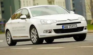 Biały Citroen C5 2.0 HDi z napisem "NOWY SILNIK 3.0 V6 HDi 240KM" na drzwiach, jadący po drodze.