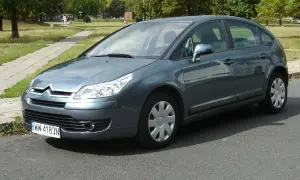 Szary Citroen C4 1.6 HDI zaparkowany przy chodniku w parku.