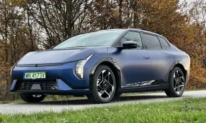 Niebieski kia sedan z matowym wykończeniem, zaparkowany na tle jesiennych drzew.