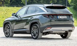 Tylna część ciemnozielonego Hyundaia Tucsona hybrydowego na żwirowej drodze. Wiele osób szuka hyundai tucson opinie przed zakupem.