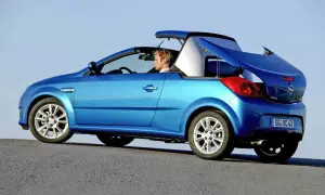 Niebieski kabriolet Opel Tigra z otwartym dachem, kierowca w środku, na tle błękitnego nieba.