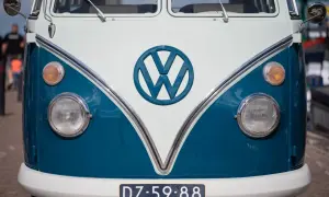 Przód klasycznego VW T2 w kolorze białym i niebieskim. Charakterystyczne okrągłe logo VW i okrągłe reflektory.
