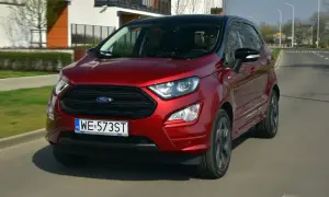 Czerwony Ford Ecosport w ruchu miejskim. Kierowca w okularach przeciwsłonecznych. Wiele pozytywnych ford ecosport opinie potwierdza jego miejski charakter.