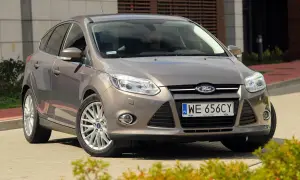 Brązowy Ford Focus MK3, często chwalony w opiniach, prezentuje się elegancko na tle nowoczesnego budynku.