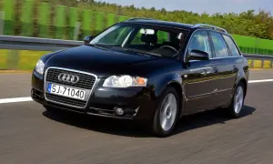 Czarne Audi A4 B7 2.0 TDI na autostradzie, z zielonymi barierami i drzewami w tle.