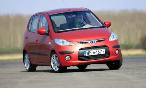 Czerwony Hyundai i10 na drodze. Kierowca w okularach i zielonym szaliku. Wiele pozytywnych hyundai i10 opinie potwierdza jego miejski charakter.