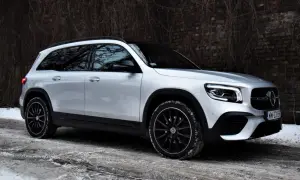 Srebrny Mercedes GLB 200 na czarnych felgach, zaparkowany na zaśnieżonej drodze przy ceglanym murze.