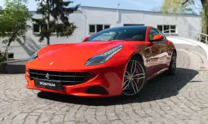 Czerwone Ferrari FF na brukowanej drodze, z widocznym logo Centrum.