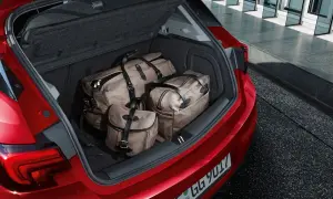 Bagażnik czerwonego Opla Astry J hatchback wypełniony trzema stylowymi torbami podróżnymi.