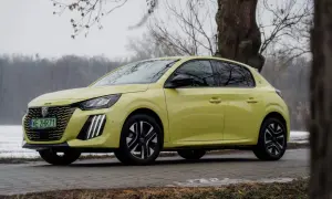 Żółty Peugeot e-208 stoi na tle drzew i zimowego krajobrazu.