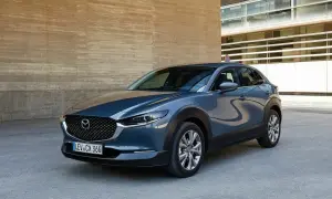 Elegancka Mazda CX-30 w szarym kolorze, zaparkowana przy nowoczesnym budynku. Choć auto prezentuje się świetnie, warto pamiętać o potencjalnych wadach Mazdy CX-30.