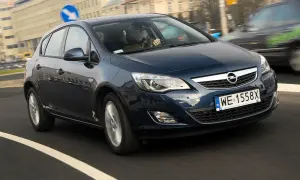 Ciemnoniebieski Opel Astra J 1.7 CDTI porusza się po miejskiej drodze. Kierowca w czapce prowadzi auto.