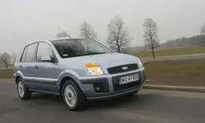 Jasnoszary Ford Fusion 1.4 benzyna jedzie po drodze. W tle drzewa i pola.