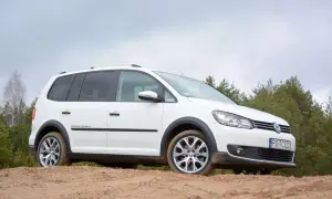 Biały VW Cross Touran na piaszczystej drodze, otoczony drzewami. Idealny do miejskich przygód i leśnych wypraw.