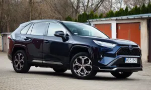 Ciemnoniebieski Toyota RAV4 Hybrid, często chwalony w toyota rav4 opinie, zaparkowany przed garażami.