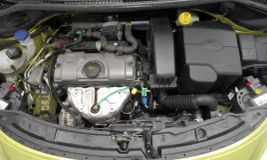 Silnik peugeot 207 1.4 benzyna. Widok komory silnika z widocznymi elementami, takimi jak alternator, obudowa filtra powietrza i zbiorniczek płynu chłodniczego.