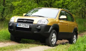 Złoty Hyundai Tucson 2007 na leśnej drodze, gotowy na przygodę.