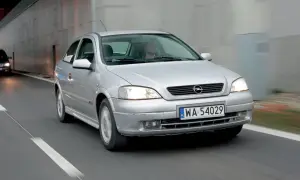 Srebrna astra 2 jedzie drogą, światła włączone, kierowca za kierownicą.