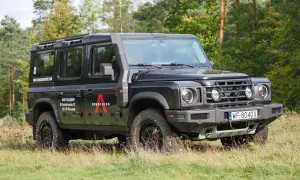 Czarny grenadier auto z bagażnikiem dachowym i snorkelami, zaparkowany na trawie wśród drzew.