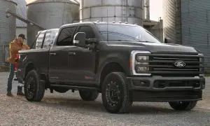 Mężczyzna ładuje pakunki do ciemnoszarego Forda Super Duty. Ciężarówka stoi na żwirowej drodze obok silosów.