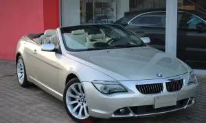 Srebrny kabriolet BMW E64 z beżowym wnętrzem stoi przed salonem samochodowym.