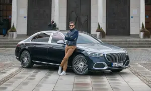 Elegancki mężczyzna opiera się o lśniącego Maybacha S580 przed monumentalnym budynkiem.