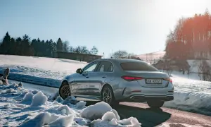 Srebrny Mercedes C 300 na tle ośnieżonych wzgórz i lasu. Zima nie straszna temu eleganckiemu autu.