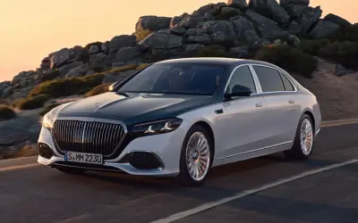 Elegancki, dwukolorowy Mercedes-Maybach sunie po górskiej drodze o zachodzie słońca.