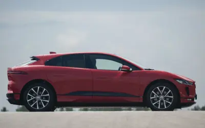 Czerwony jaguar elektryczny w profilu, z widokiem na jego aerodynamiczną sylwetkę i felgi.