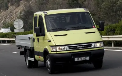 Żółty Iveco Daily 3 z podwójną kabiną i skrzynią ładunkową jedzie po drodze.
