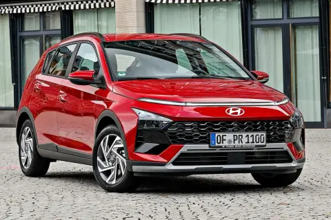 Czerwony Hyundai Bayon z nowoczesnym designem, błyszczącym lakierem i charakterystycznym grillem, zaparkowany na brukowanej ulicy.