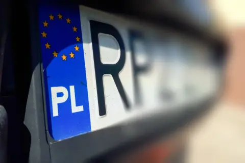 Zbliżenie na polską tablicę rejestracyjną z symbolem Unii Europejskiej. Litery "PL" i fragment kolejnych znaków są wyraźne, reszta rozmyta.