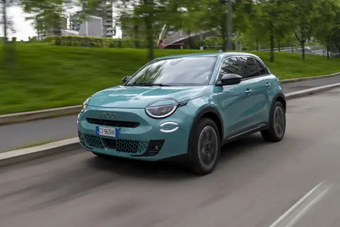 Nowoczesny, turkusowy Fiat 600 Hybrid sunie po miejskiej drodze, otoczony zielenią i budynkami.