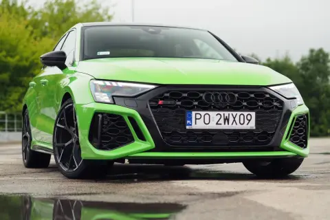 Jaskrawozielone Audi RS3 Sedan z czarnymi felgami stoi na mokrej nawierzchni, odbijając się w kałużach.