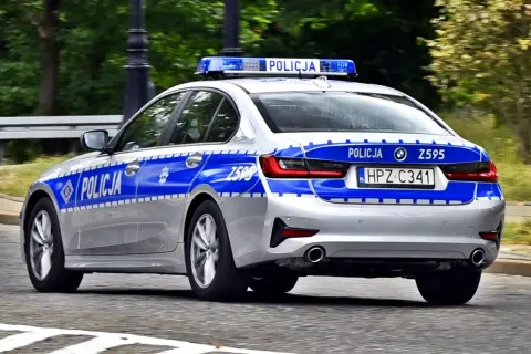 Srebrny radiowóz policyjny z niebieskimi pasami i napisem "POLICJA" na drzwiach i tyle. Widoczna tablica rejestracyjna HPZ C341.
