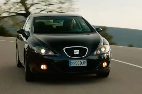 Czarny Seat Leon 2 jedzie po krętej drodze wśród drzew.