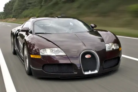 Ciemnobrązowy Bugatti Veyron pędzi po drodze. Jego cena jest astronomiczna, ale osiągi zapierają dech w piersiach.