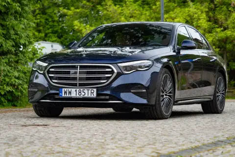 Elegancki, ciemnogranatowy Mercedes e300 lśni po deszczu na tle zieleni.