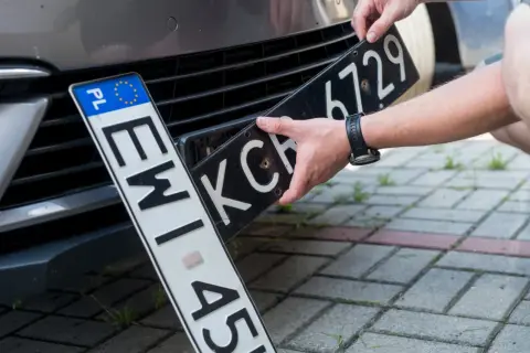 Ręce montują tablicę rejestracyjną do samochodu. Nowa elc rejestracja czeka na zamontowanie.