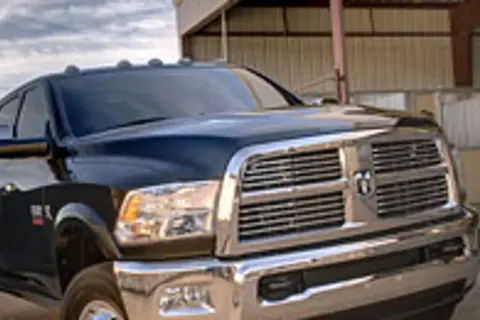Ciemny Dodge Ram 3500 z chromowanym grillem i błyszczącym lakierem stoi przed budynkiem.