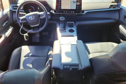 Wnętrze Toyoty Sienna Hybrid: czarne skórzane fotele, kierownica, deska rozdzielcza z ekranem nawigacji.