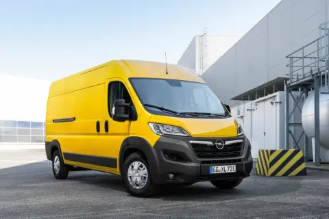 Żółty Opel Movano stoi na parkingu przed nowoczesnym budynkiem przemysłowym.