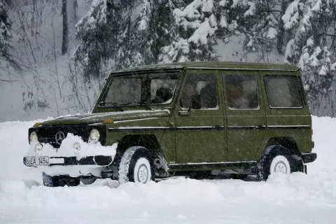 Zielony Mercedes G-klasa z napędem **awd** przebija się przez zaspy w zaśnieżonym lesie.