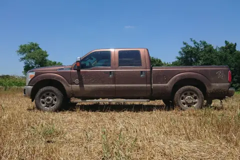Brązowy Ford F250, ubrudzony ziemią, stoi na polu z suchą trawą.