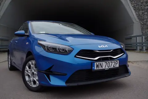 Niebieska Kia Ceed 1.5 T-GDI z nowoczesnymi światłami i grillem, zaparkowana przy betonowym tunelu.