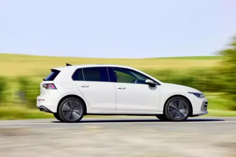 Biały hatchback pędzi po drodze, otoczony rozmytymi zielonymi polami i błękitnym niebem.