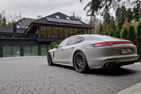 Białe Porsche Panamera GTS przed nowoczesnym budynkiem z panelami słonecznymi. Idealny wybór dla firm ceniących leasing operacyjny.